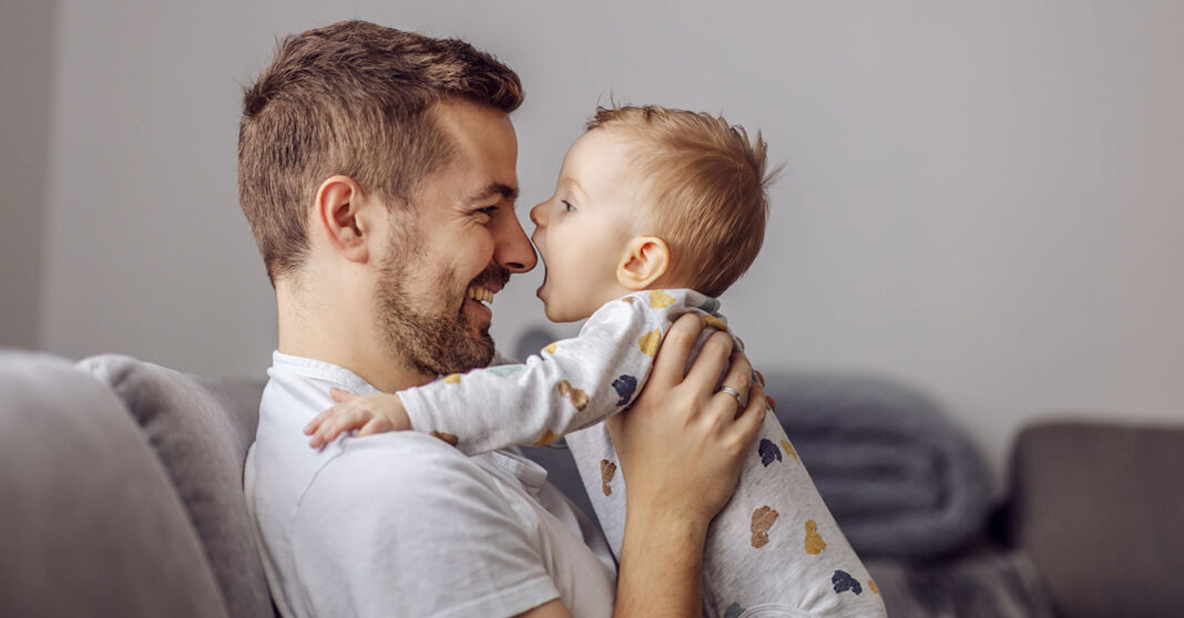 Fiatal apuka a kisfiával játszik, a gyerek épp készül bekapni az orrát