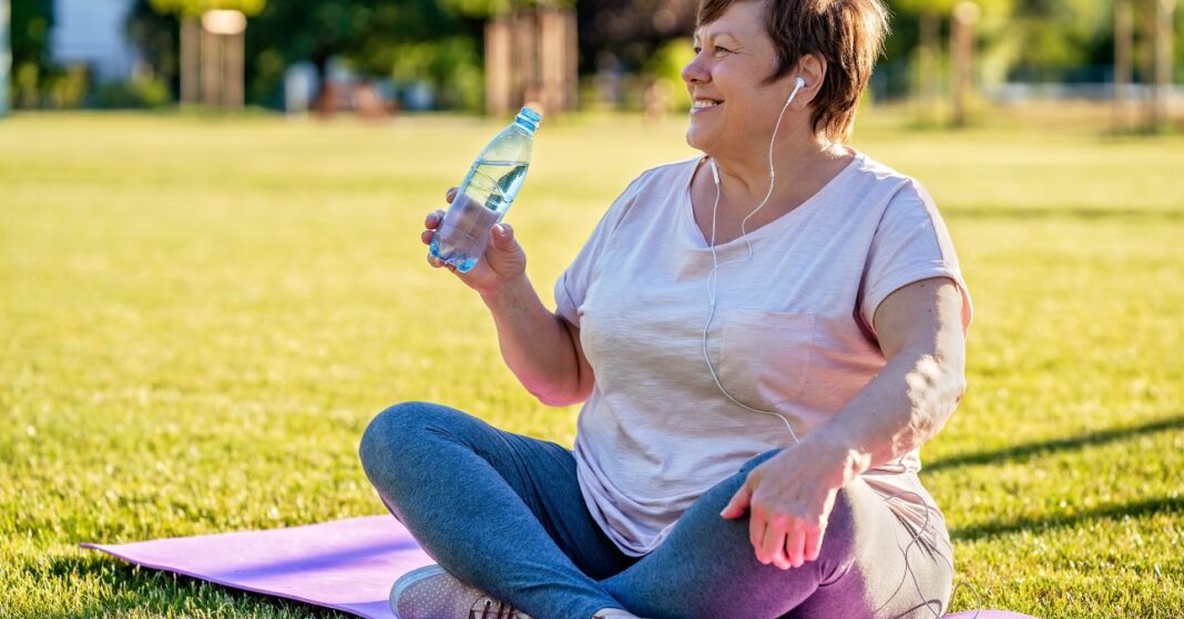 menopauza idős nő jógamatracon ül és vizet iszik
