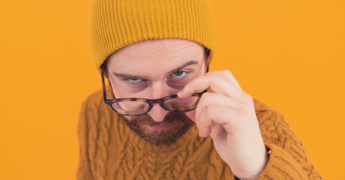 fiatal férfi kérdőn néz ki a szemüvege fölött