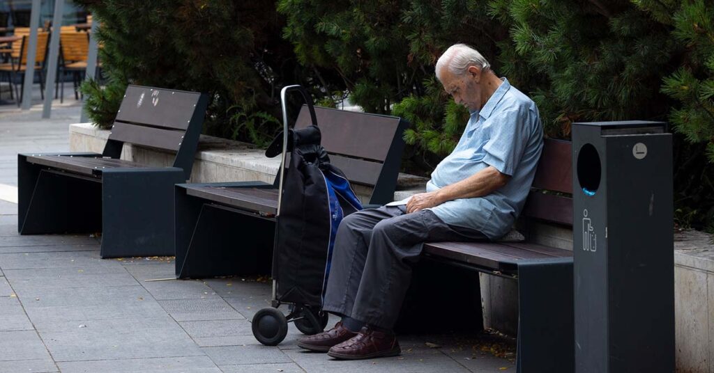 idős nyugdíjas férfi padon ül, maga elé néz, mellette banyatank