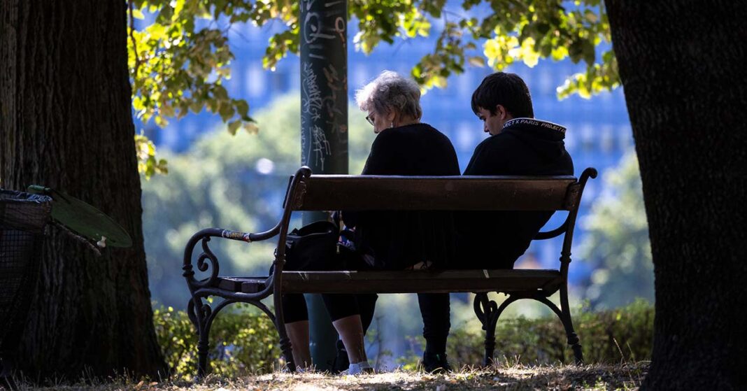 nyugdíjas és fiatal ül egymás mellett egy padon napsütésben