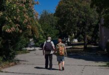 idősek sétálnak egy parkban nyáron hátizsákkal
