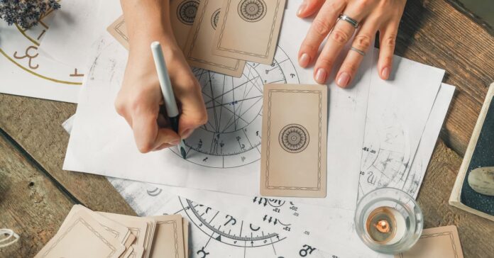 asztrológiai előjelzést készít egy nő csillagtérképpel, körülötte kártyák és gyertya