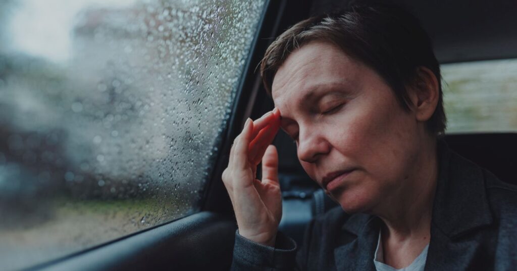 nő fejfájással autó hátsó ülésén ül esős időben