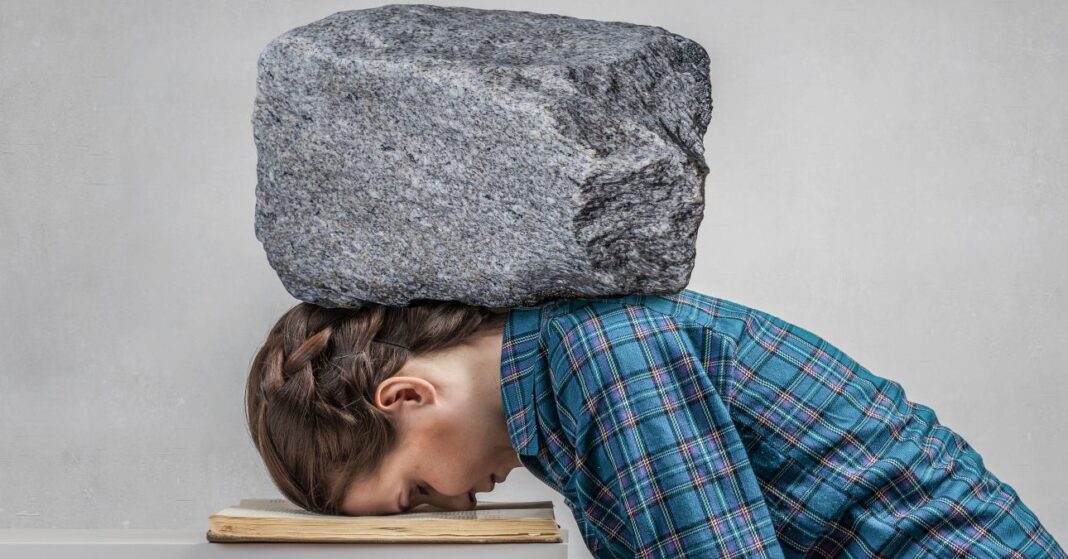 fejfajas fiatal lány arccal könyvre dőlve, nyakán ás vállán nagy szürke kő