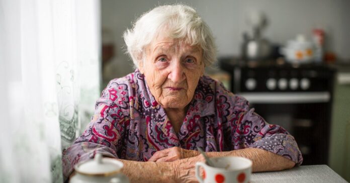 idős, nyugdíjas nő ül a konyhájában, piros pöttyös bögre előtte