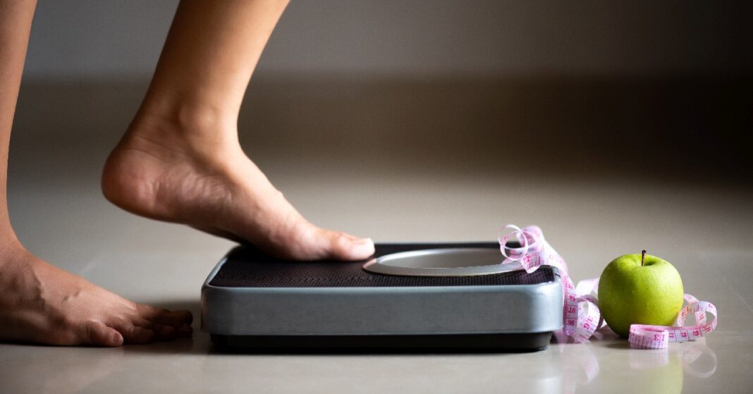 női láb, jobb lábbal a mérlegre lép, előtt alma és mérőszalag