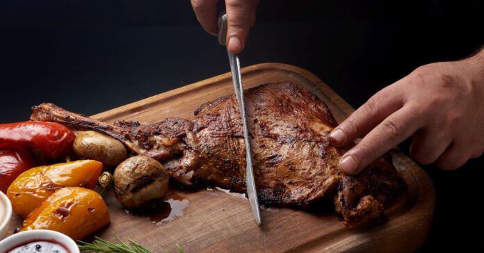 Marton-napi sült libát szel kettő egy férfi kéz vágódeszkán, mellette gomba, mártás