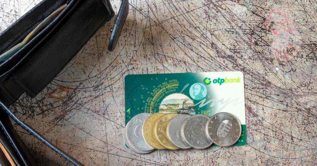 SZÉP-kártya egy karcos asztalon, rajta 10, 20 és forintos érmékkel, mellette kinyitott pénztárca