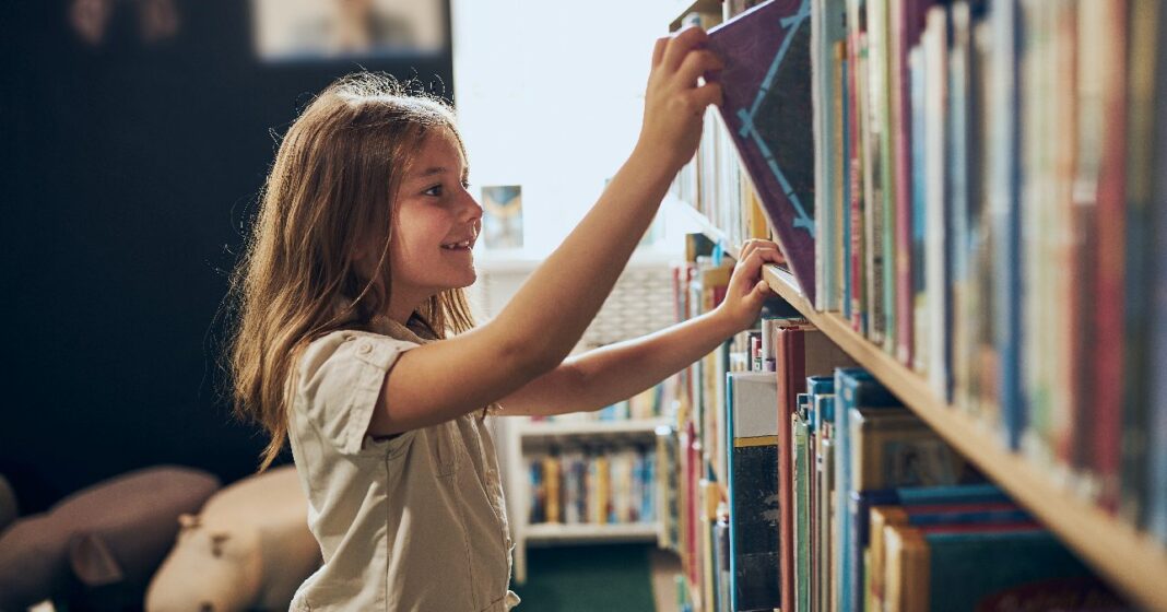 kislány az iskolai könyvtárban könyvet emel le a polcról