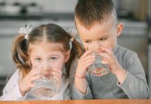 Iszol te eleget? Folyadékbevitel-kalkulátor a Hóvégén kislány és kissrác egy-egy pohár vizet iszik, kislány a kamerába néz, kisfiú félszemmel a lányra