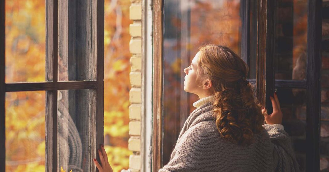 Fiatal nő néz ki a nyitott ablakon ősszel