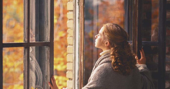 Fiatal nő néz ki a nyitott ablakon ősszel