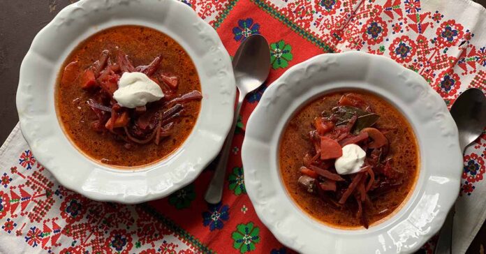 Borscs leves fehér porcelán tányéron, tetején tejföllel