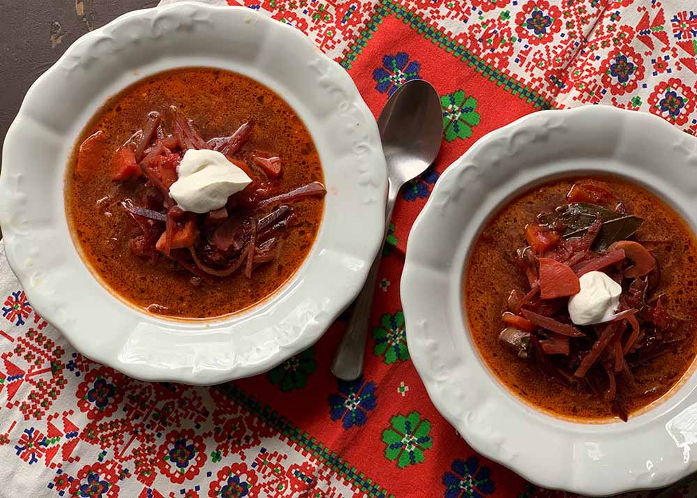 Borscs leves fehér porcelán tányéron, tetején tejföllel