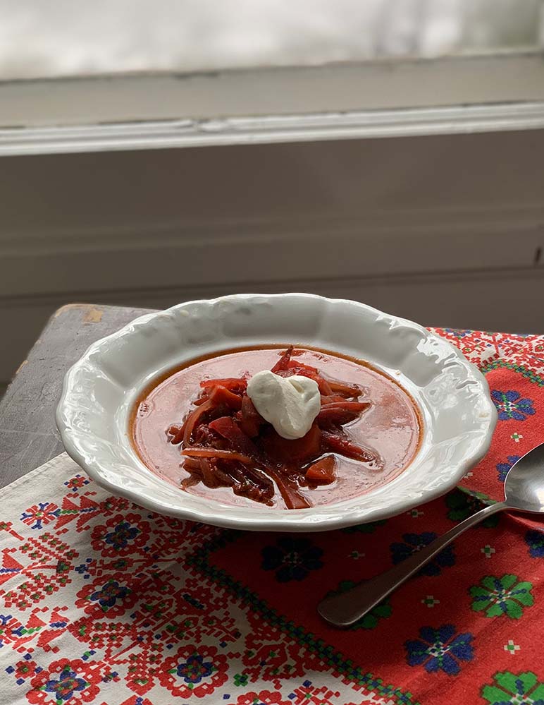 Borscs leves fehér porcelán tányéron, tetején tejföllel