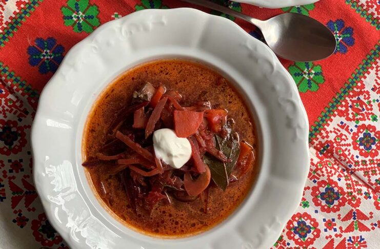 Borscs leves fehér porcelán tányéron, tetején tejföllel