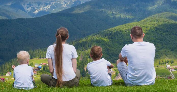 Család: két kisgyermek, anya és apa kiránduláson a hegyekben, a fűben ülnek