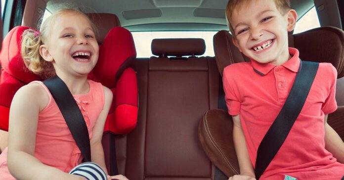 Két gyermek gyerekülésben mosolyog az autóban