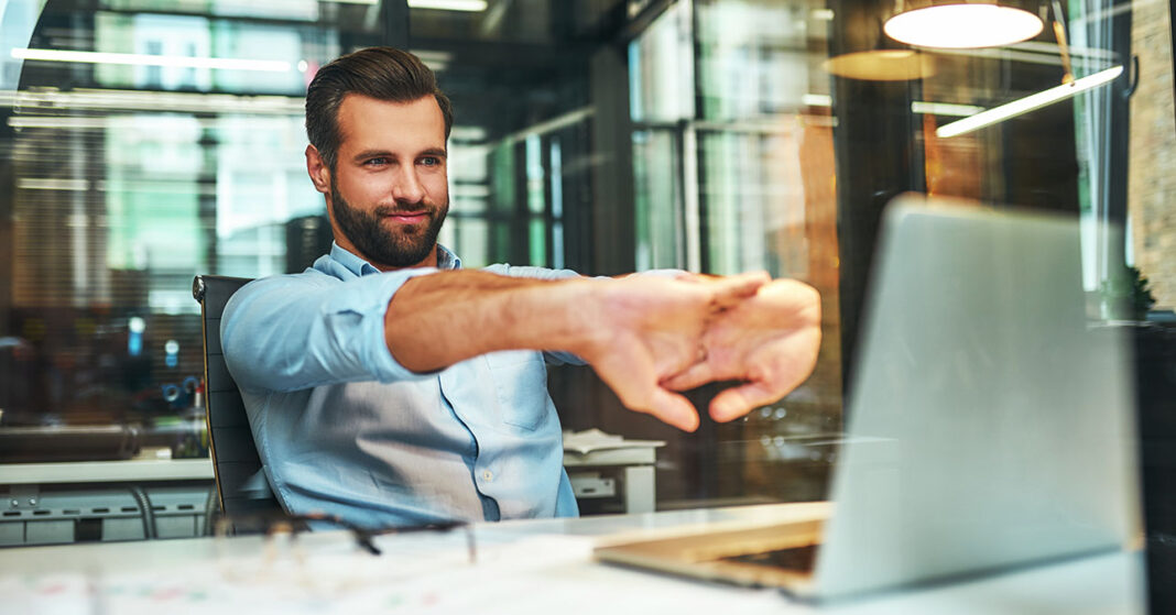 Sikeres férfi a munkahelyén számítógéppel, összefonott ujjakkal, elégedett a munkájával
