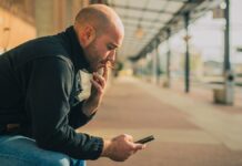 vasútállomáson fiatal, kopasz férfi padon ülve dohányzik