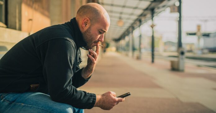 vasútállomáson fiatal, kopasz férfi padon ülve dohányzik