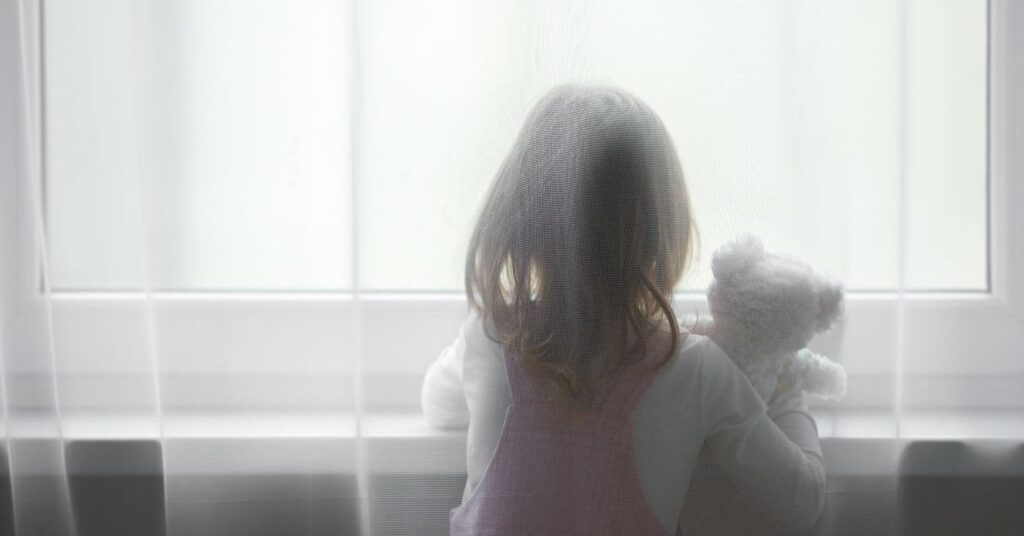 Kislány az ablakban a macijával.