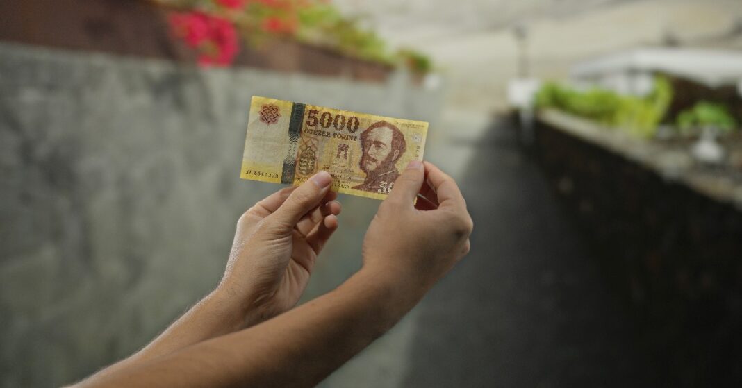 férfi 5000 forintos bankjegyet tart a kezében az utcán