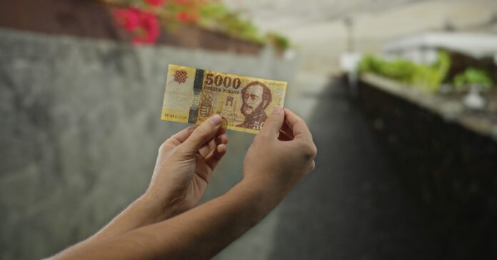 férfi 5000 forintos bankjegyet tart a kezében az utcán