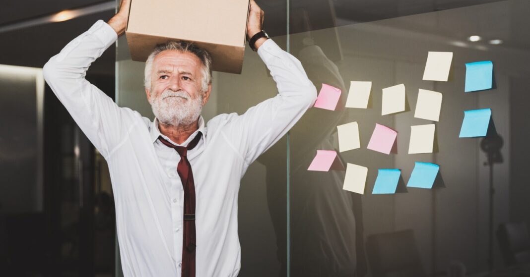 Egy őszhajú férfi dobozzal a kezében csalódottan a munkahelyén