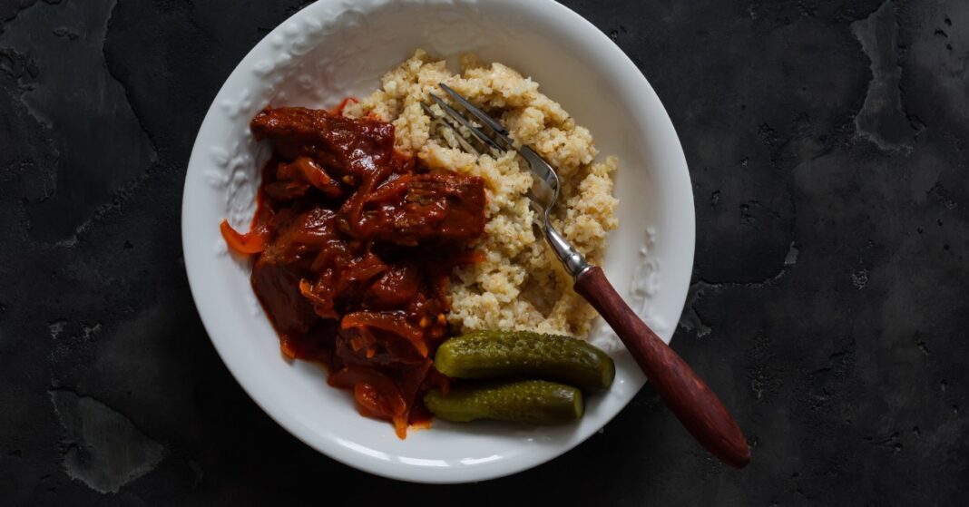 pörkölt és kovászos uborka fehér tányéron