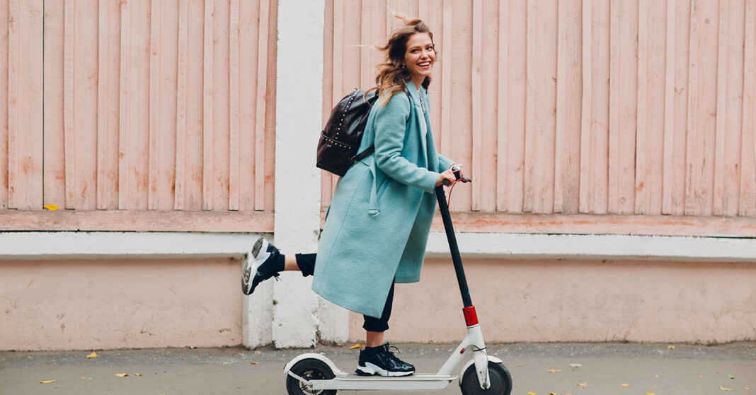 Fiatal nő kék kabátban elektromos rolleren utazik