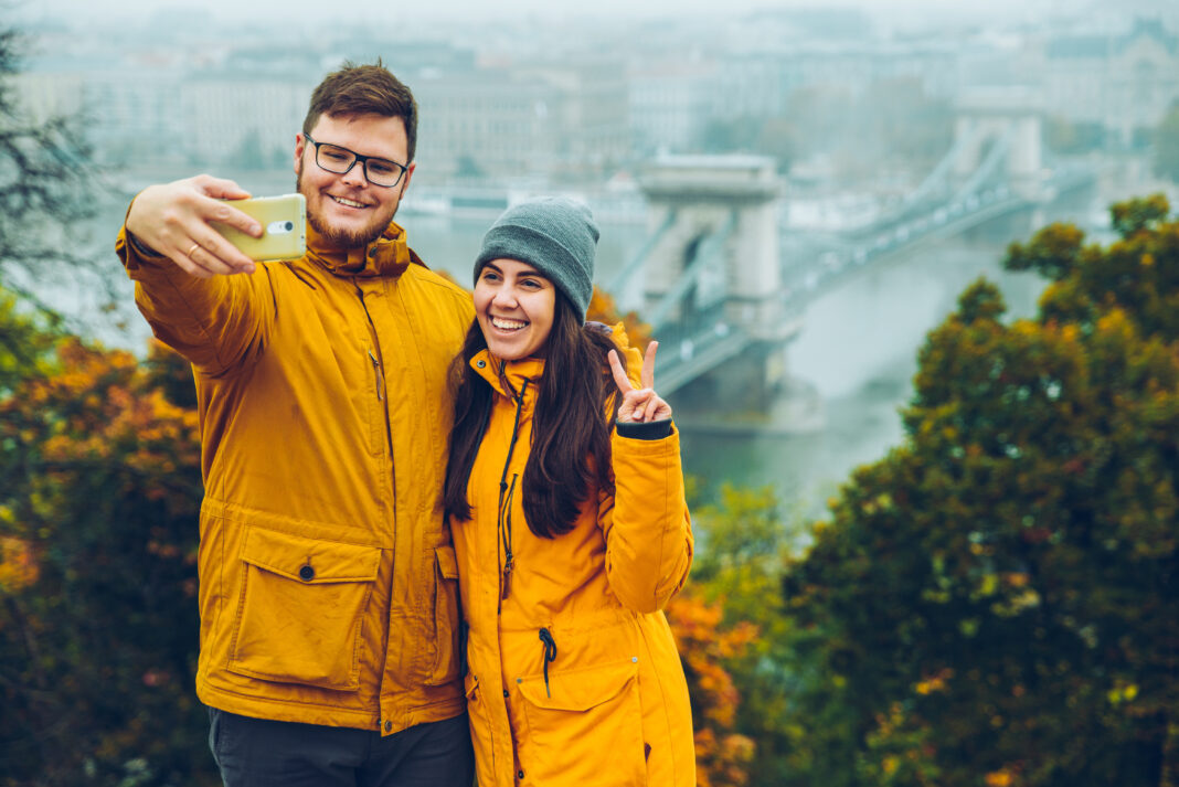Egy kedves férfi és nő telefonnal szelfizik budapesti háttér elől