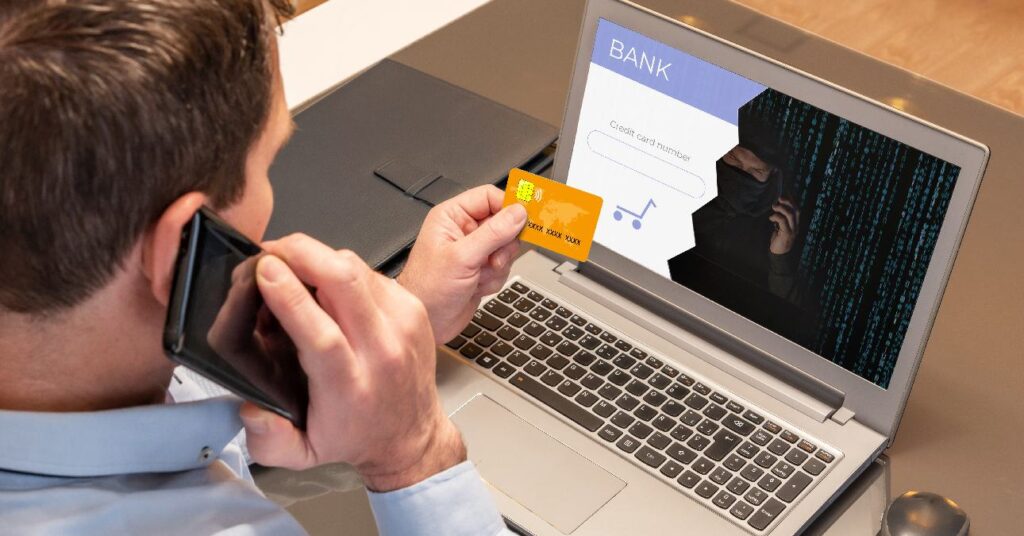 Egy férfi a bankkártyájával online vásárol a laptopja előtt, a képernyőn félig látszik egy csaló
