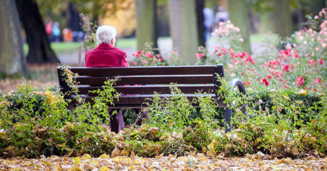 Magányos nyugdíjas nő egyedül ül a parkban egy padon